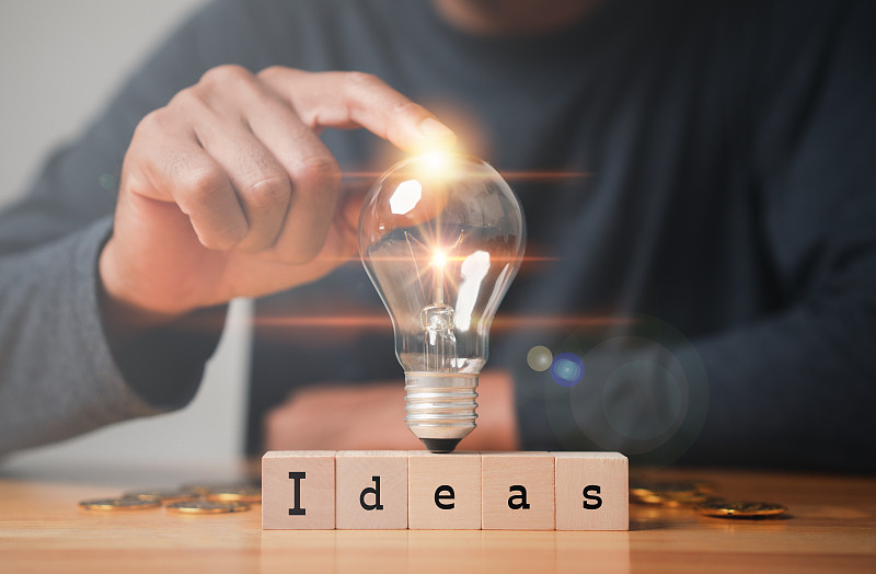 以创新和灵感为理念的新理念。用Word创意，创新科技和传播理念，触摸木块上的灯泡。图片下载
