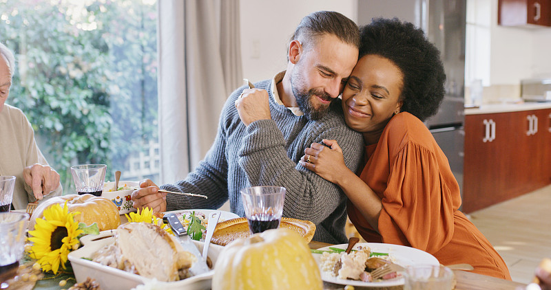食物，夫妻和爱，一个女人和男人拥抱在一起吃饭和享受在一个家庭访问。快乐，微笑和多样性的男性和女性坐在桌旁拥抱图片下载