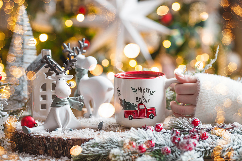一张有可爱驯鹿的圣诞卡和一杯以美丽的焦景为背景的热咖啡。新年静物画。家庭度假的概念，温馨和舒适。图片下载