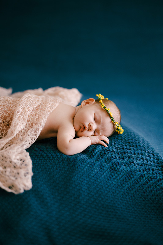 戴着黄色花环的婴儿裹着粉红色的披肩睡觉图片下载