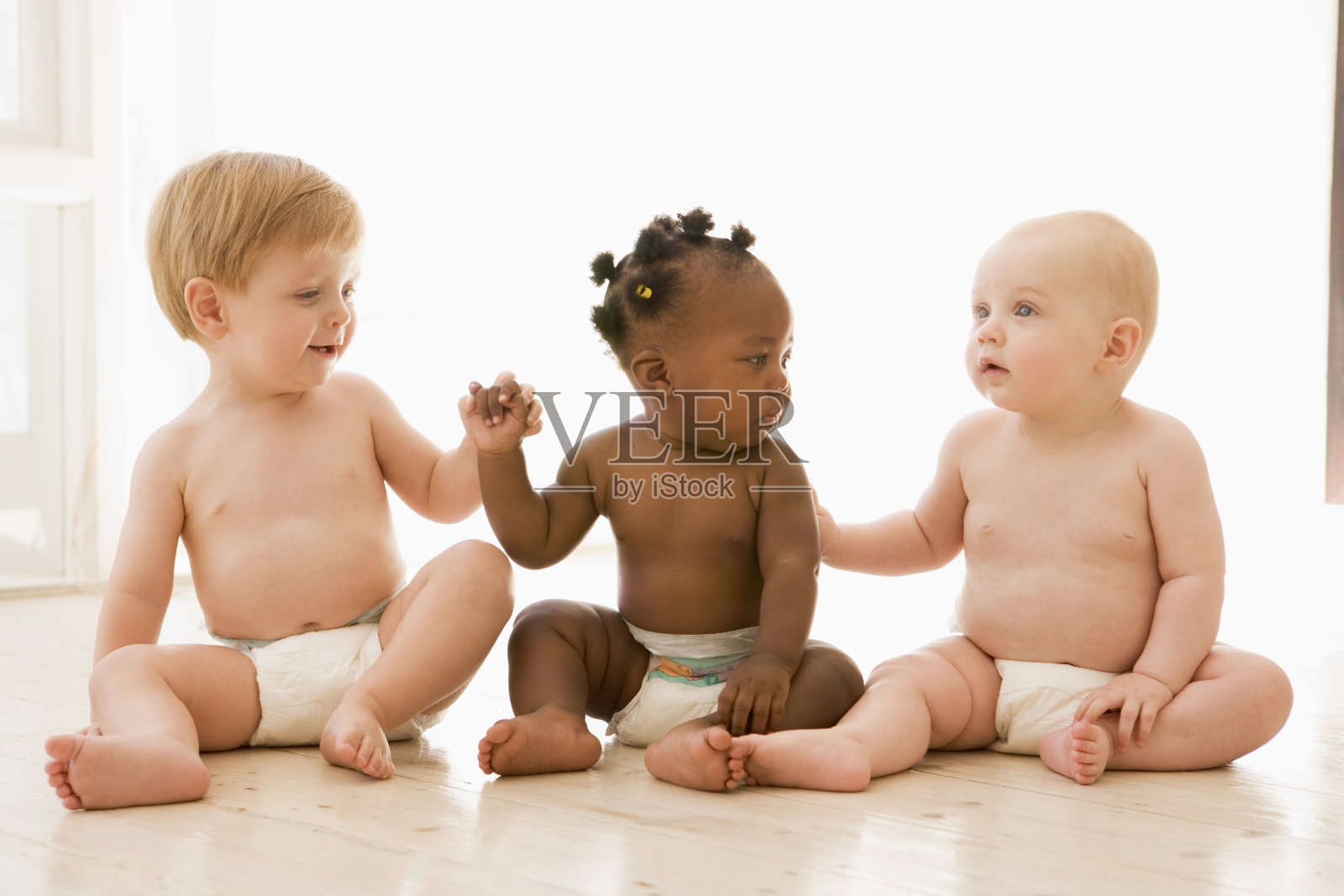 三个婴儿手牵着手坐在屋里照片摄影图片