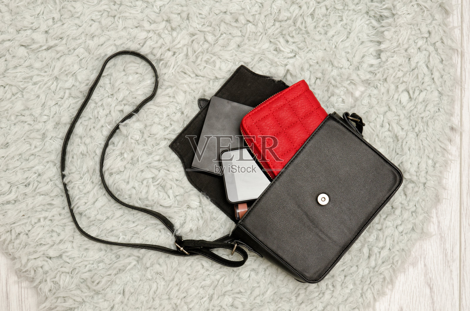 打开黑色手提包，红色钱包，手机和口红在里面。灰色毛皮背景，俯视图。时尚的概念照片摄影图片