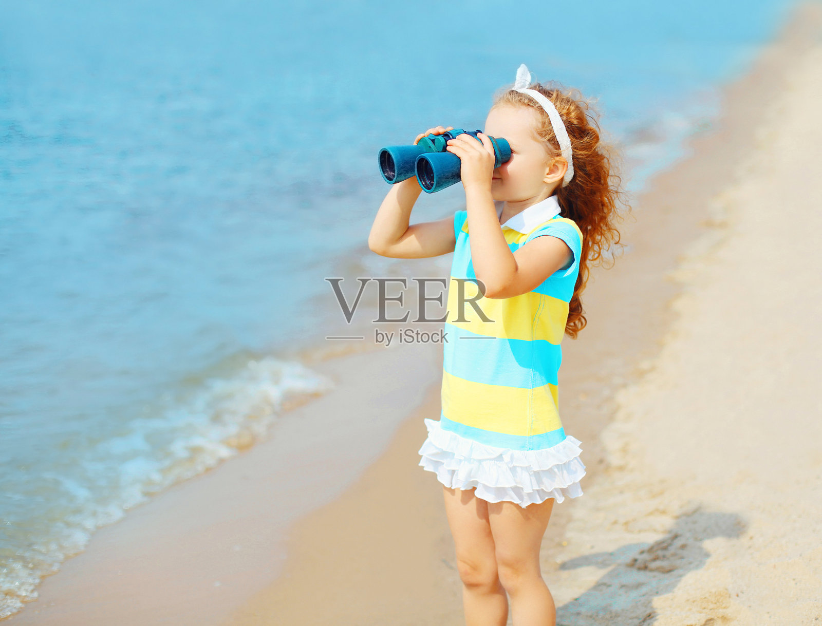 一个小女孩在海边的海滩上用双筒望远镜看着照片摄影图片