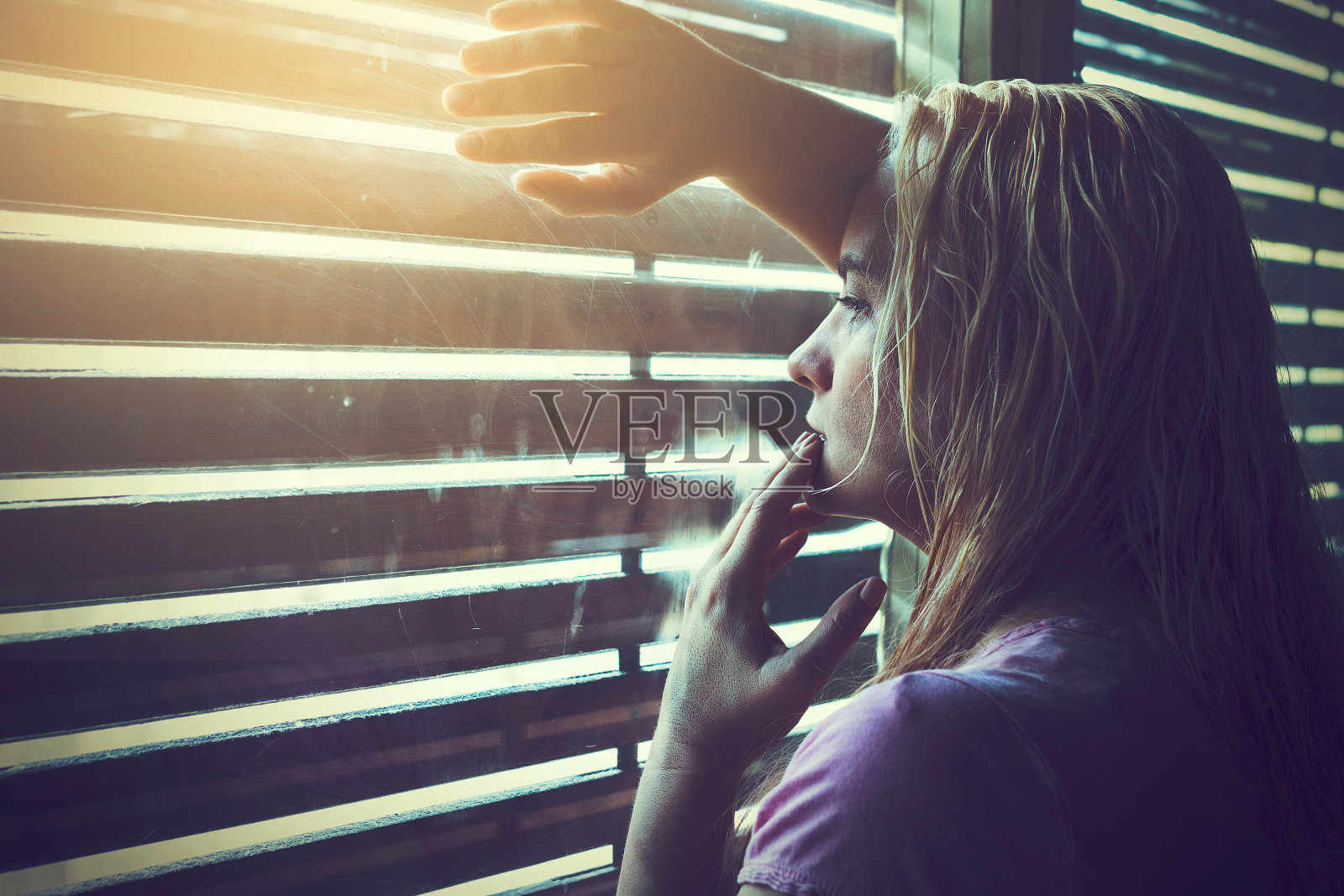 悲伤孤独的金发女人透过百叶窗看照片摄影图片