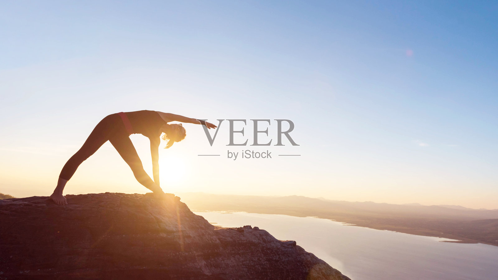 日落时分，年轻女子站在山上练瑜伽。照片摄影图片