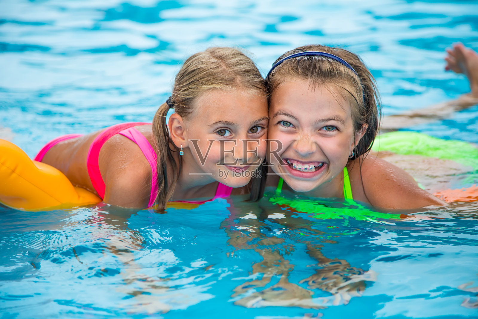 两个快乐的女孩在阳光明媚的日子里在游泳池里玩。照片摄影图片