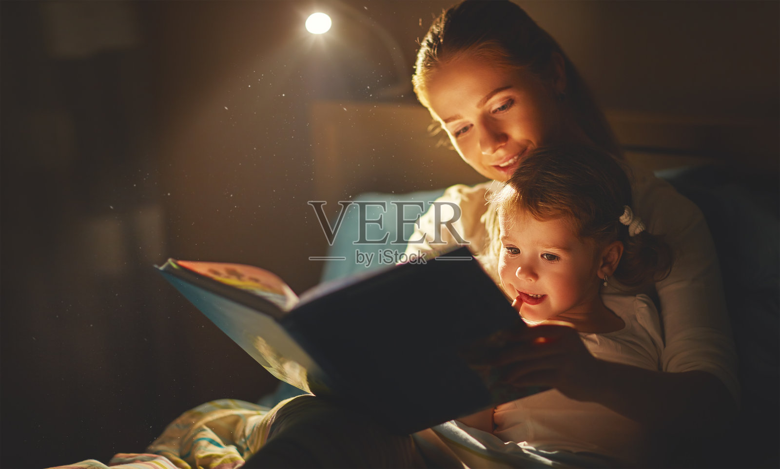 妈妈和小女孩在床上看书照片摄影图片
