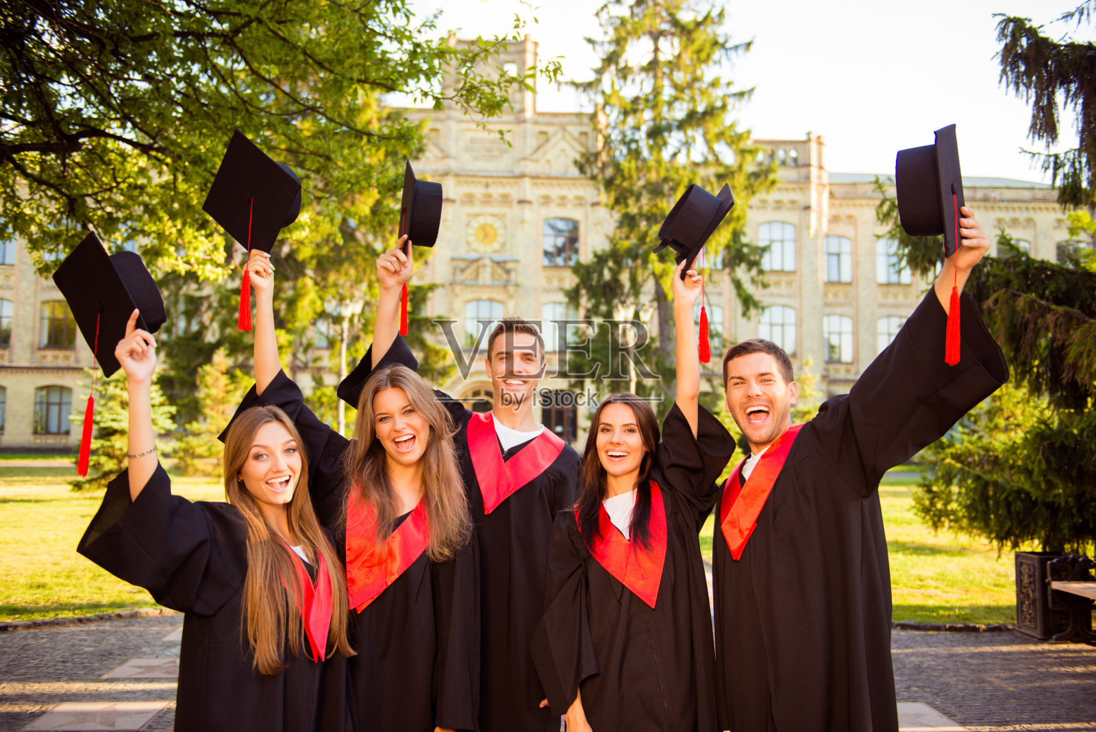 成功快乐的五名毕业生穿着长袍一起举起学位帽照片摄影图片