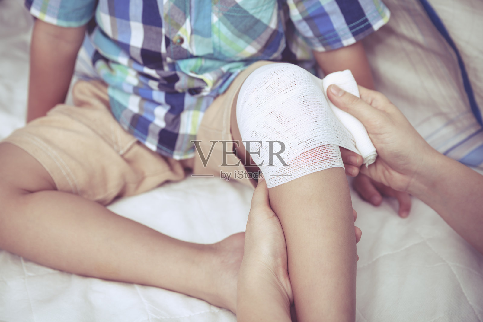 孩子受伤。母亲在包扎儿子的膝盖。复古风格。照片摄影图片