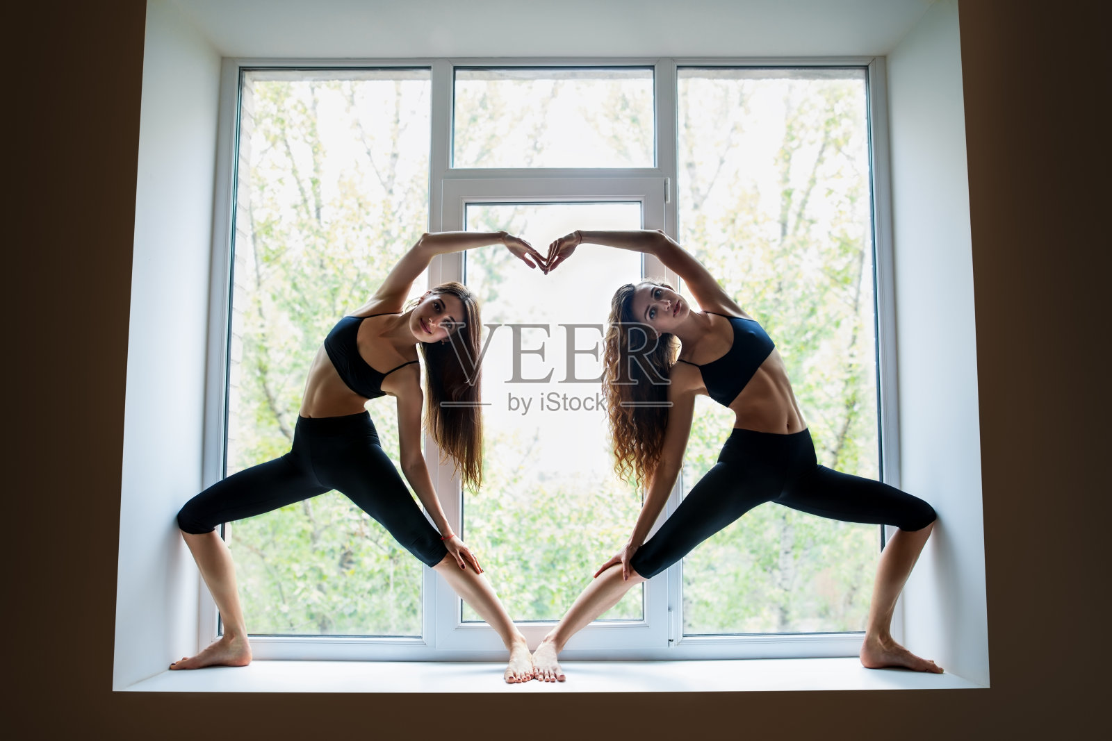 两个美丽的女人在做瑜伽体式，窗台上显示心形符号照片摄影图片