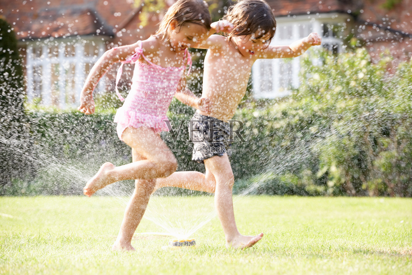 两个孩子穿过花园洒水器照片摄影图片