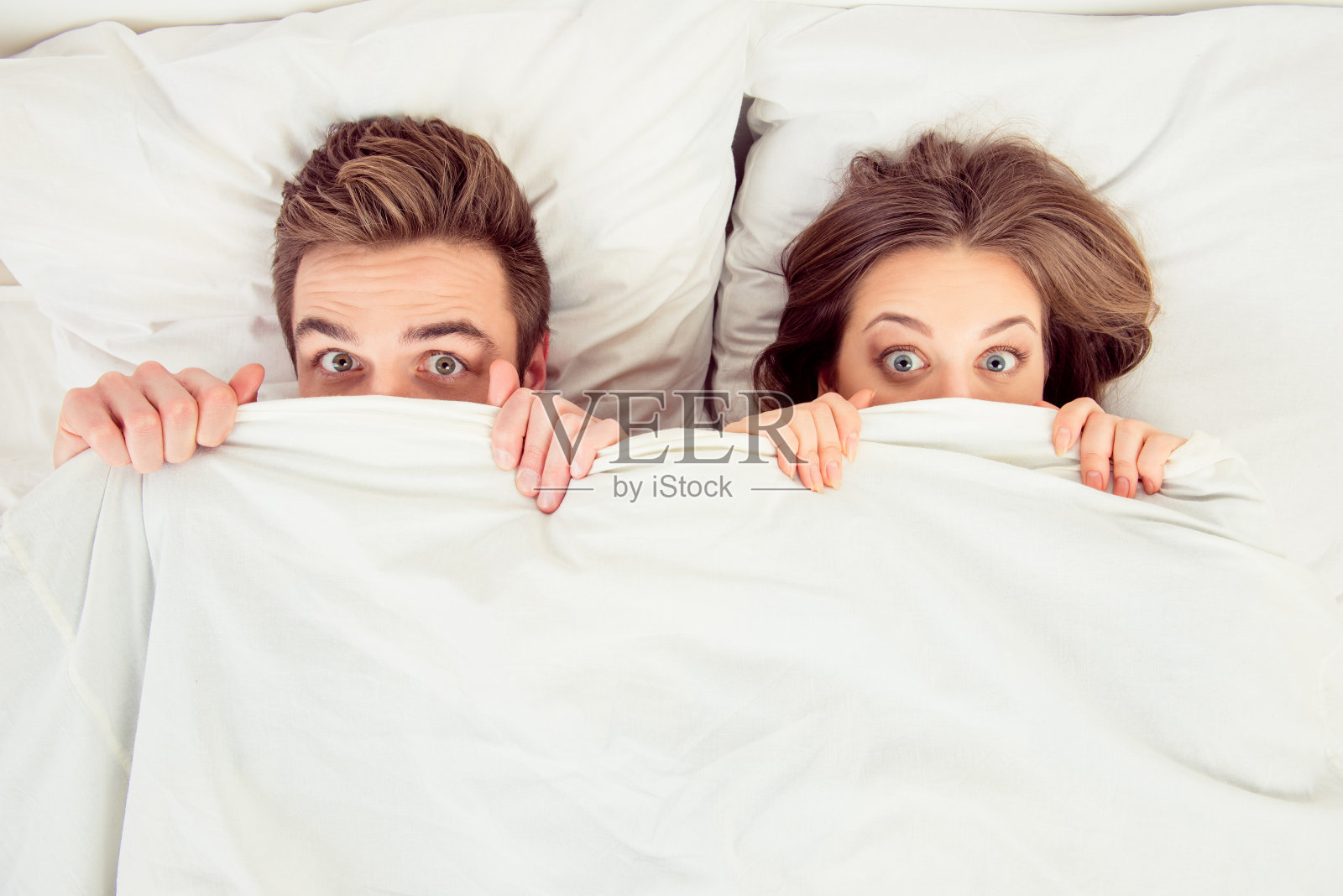 在床上盖着毯子，惊讶有趣的相爱的夫妇照片摄影图片