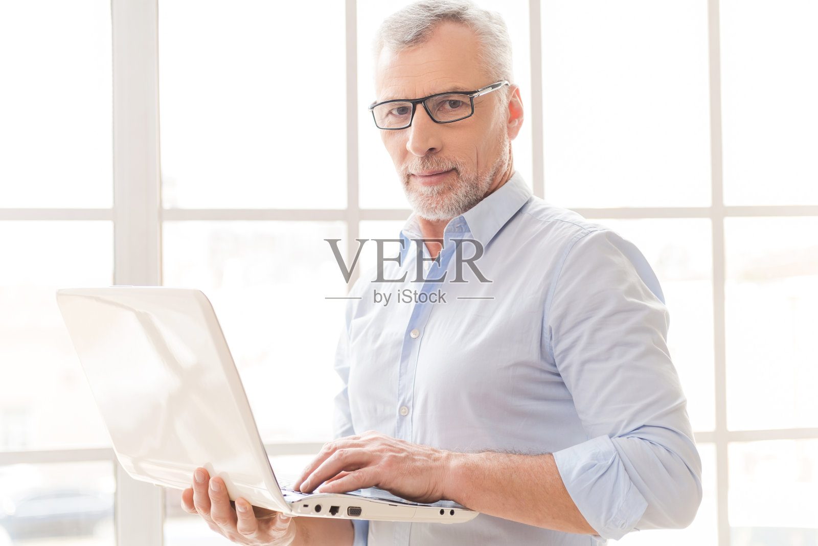戴眼镜的男人站在窗边用笔记本电脑照片摄影图片
