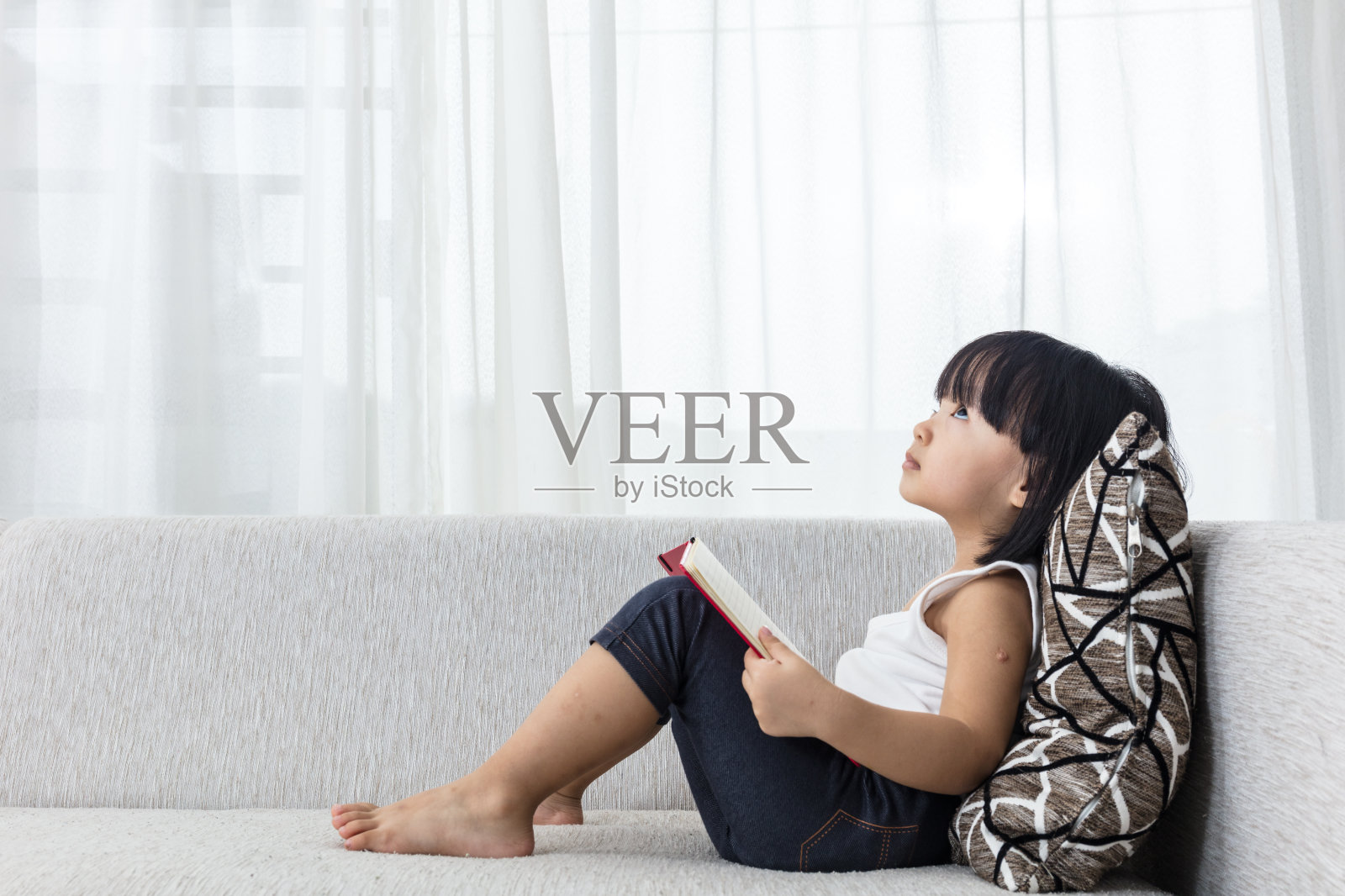 亚洲华人小女孩在沙发上一边看书一边思考照片摄影图片