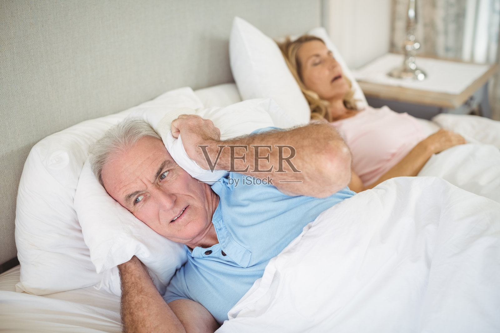 老人躺在床上，用枕头捂着耳朵照片摄影图片