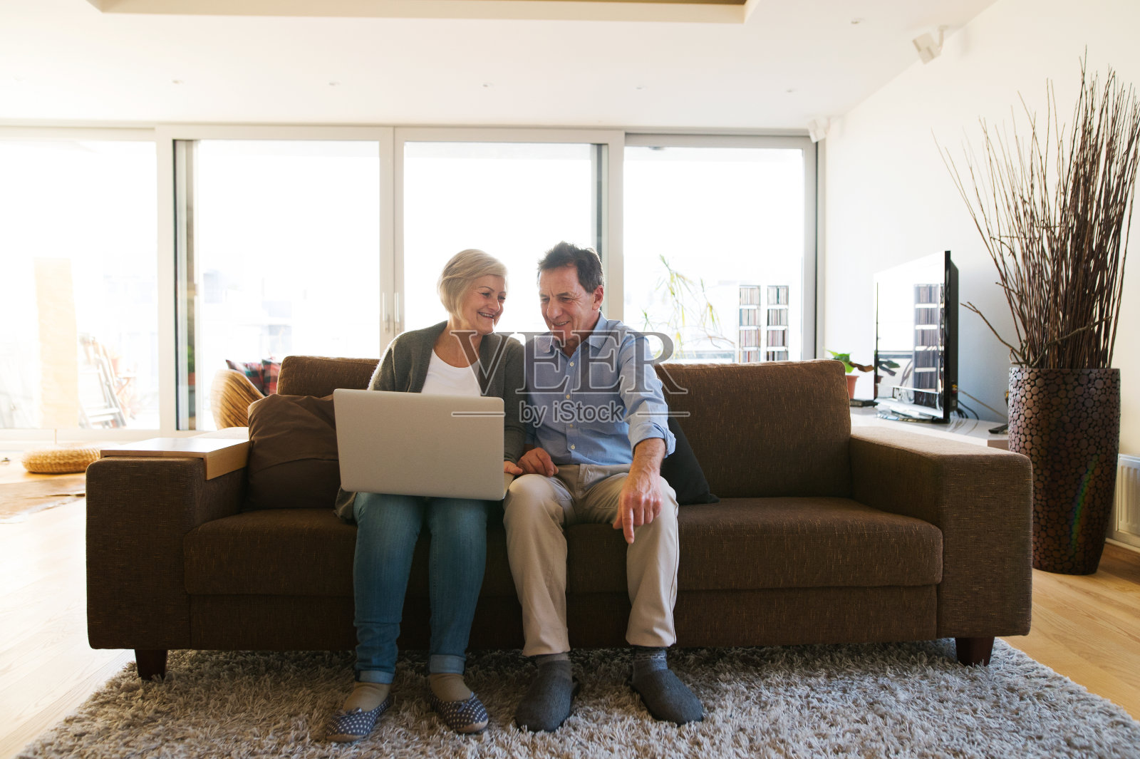 一对老年夫妇坐在客厅的沙发上，拿着笔记本电脑照片摄影图片
