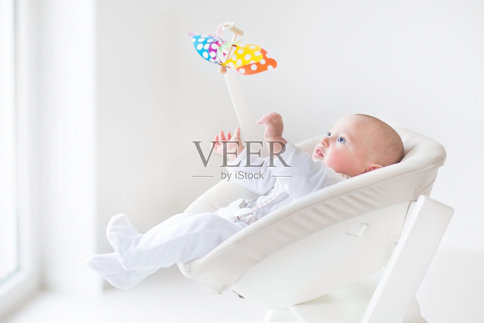可爱的新生儿在白色的椅子上看彩色的移动玩具照片摄影图片
