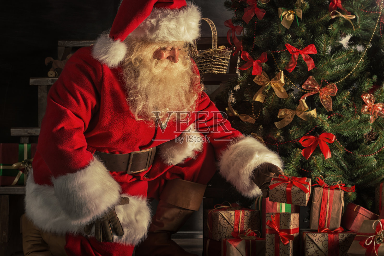 圣诞老人正在把礼物盒放在圣诞树下照片摄影图片