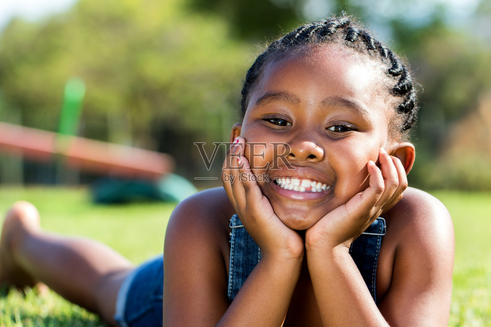 一个非洲女孩躺在公园里，双手捂住脸。照片摄影图片