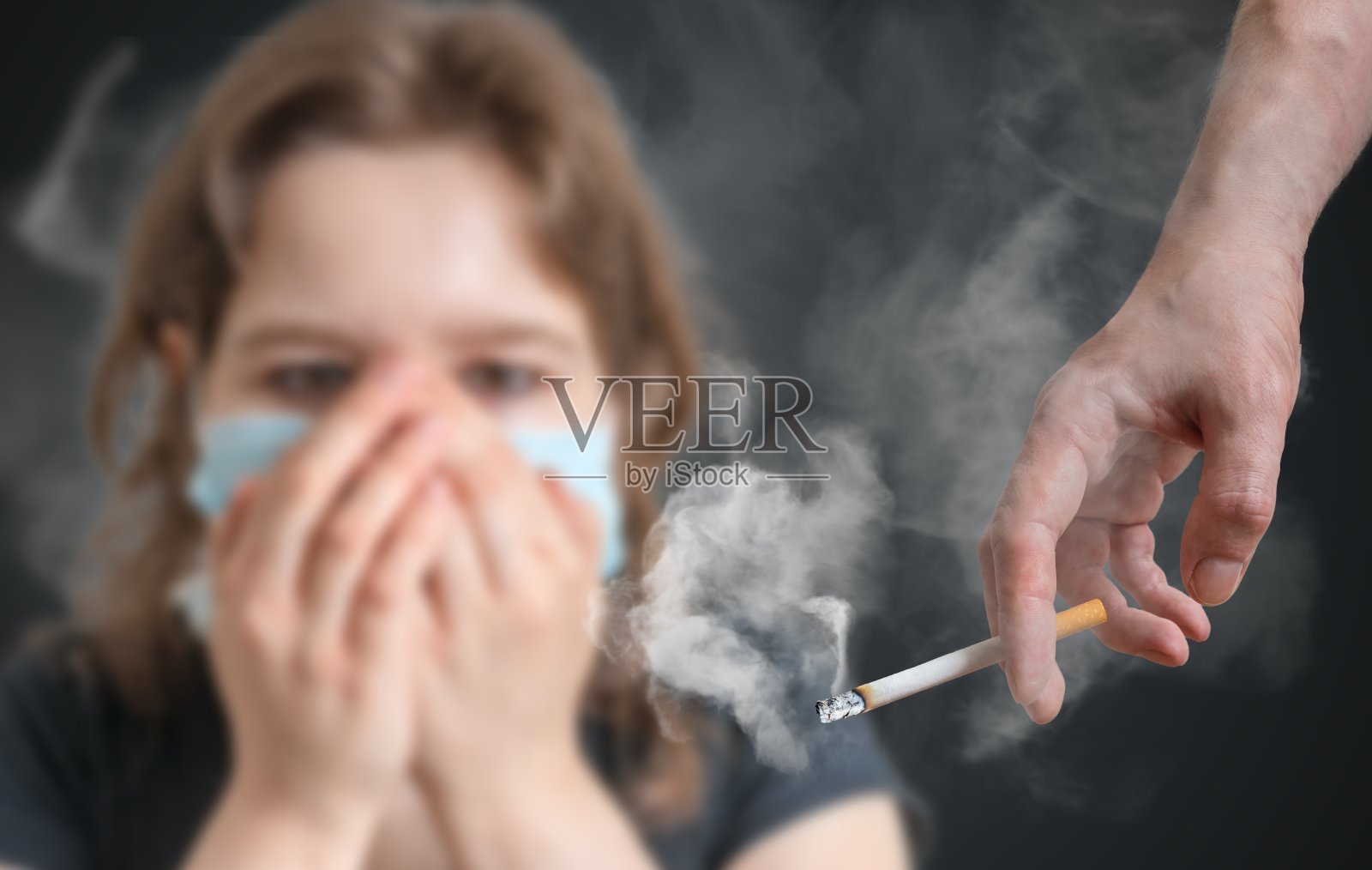 被动吸烟的概念。那个女人正捂着脸躲避香烟的烟雾。照片摄影图片