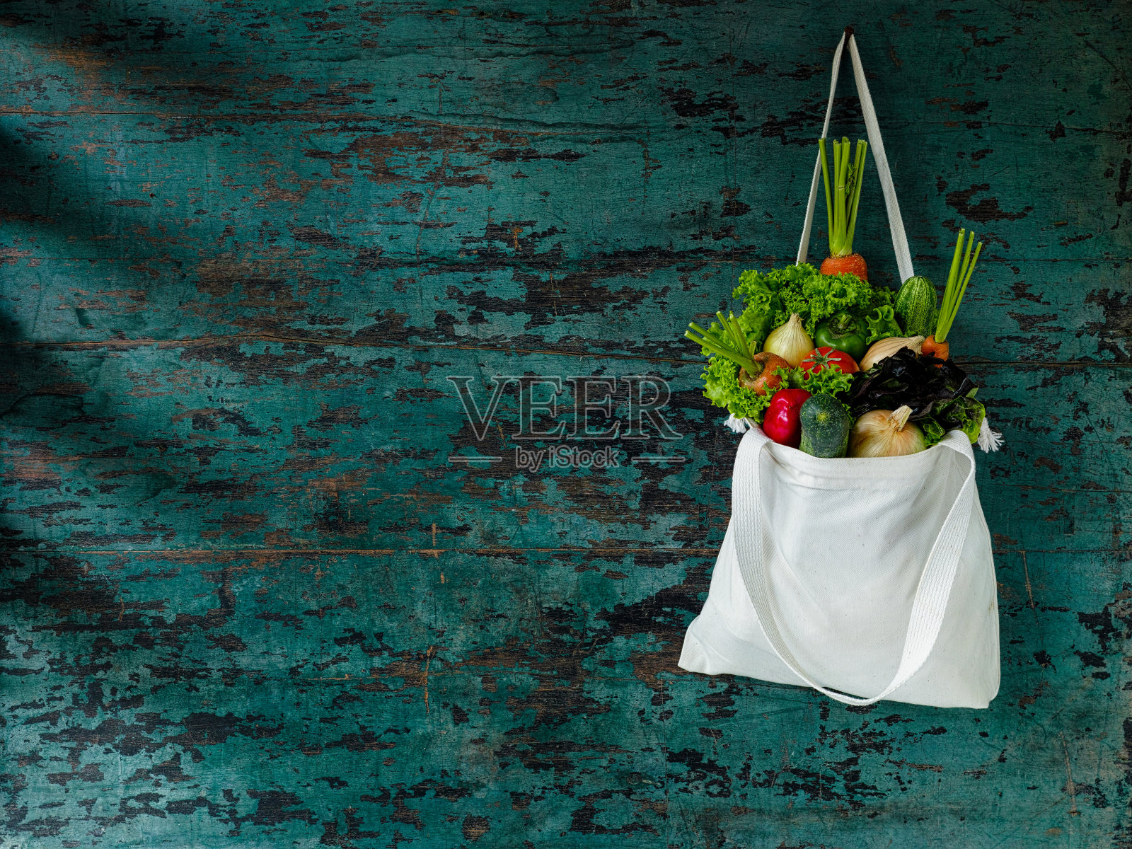 市场新鲜的沙拉蔬菜挂在一个天然棉花可回收的购物袋，用钉子挂在旧木绿松石色的墙壁上。照片摄影图片