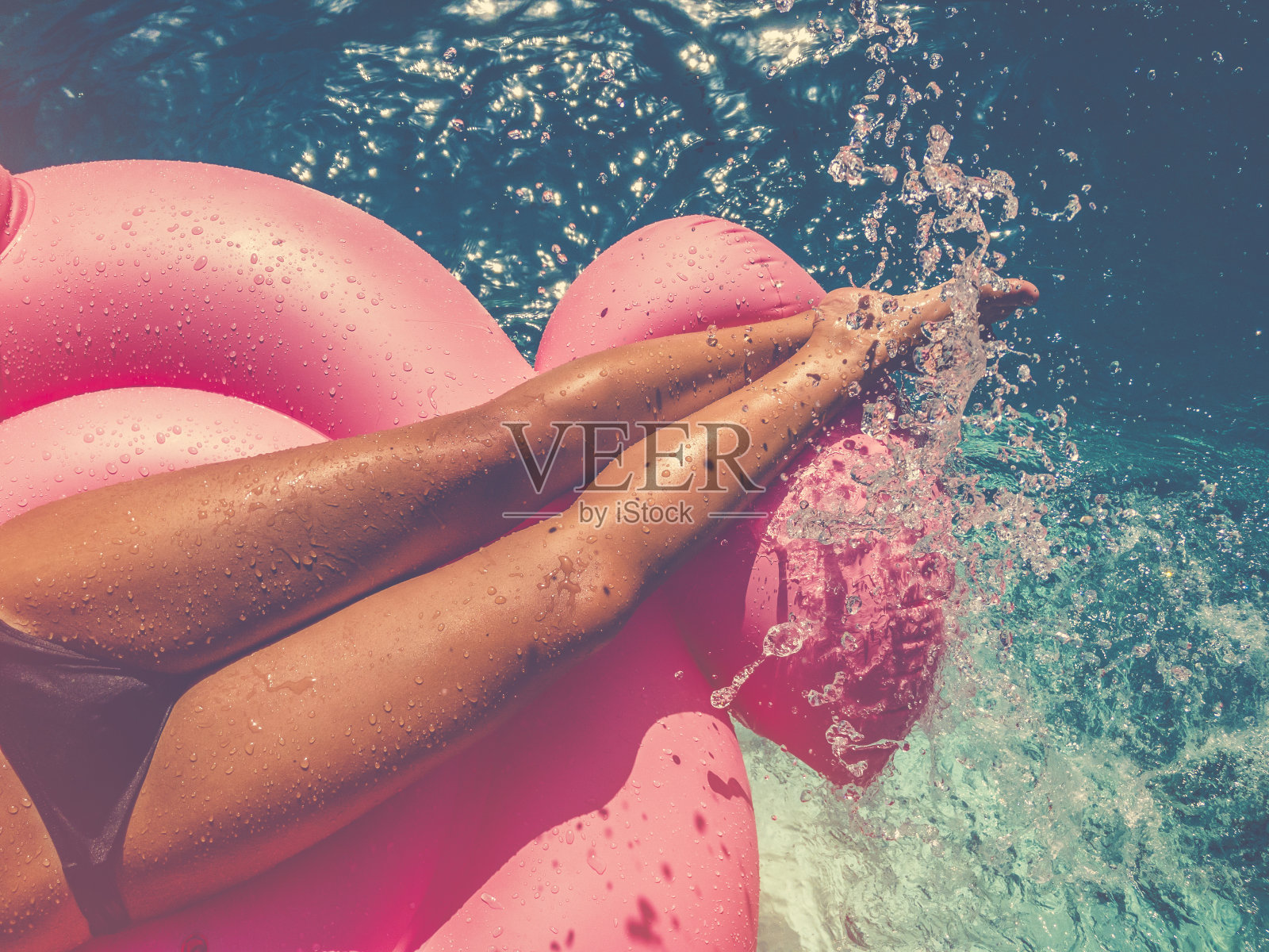一个女人在游泳池里漂浮在粉红色的充气上。照片摄影图片