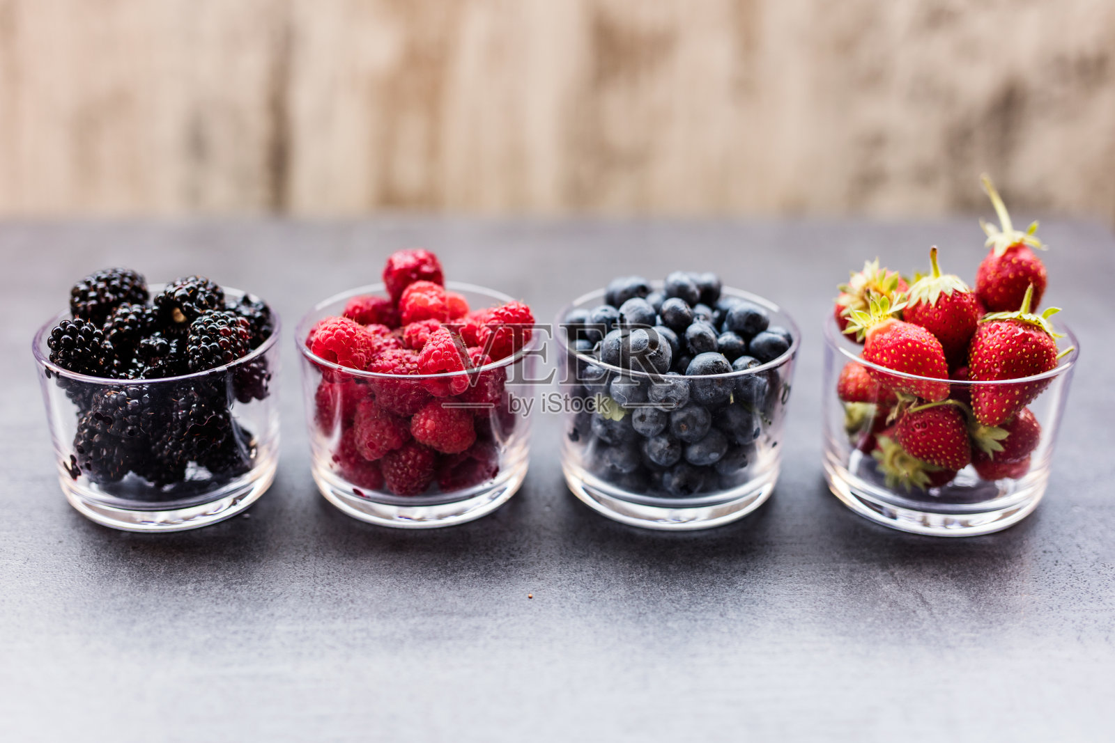 四个盛满夏季浆果的碗，比如草莓、覆盆子、蓝莓和黑莓。照片摄影图片