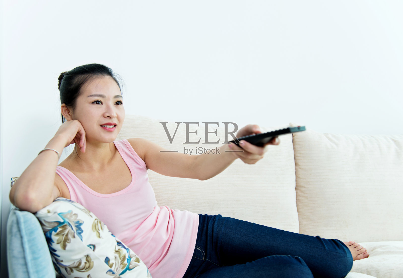 年轻的亚洲女人用遥控器在沙发上看电视照片摄影图片