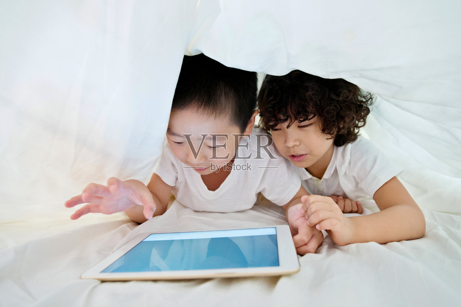 两个男孩在被窝里用平板电脑照片摄影图片