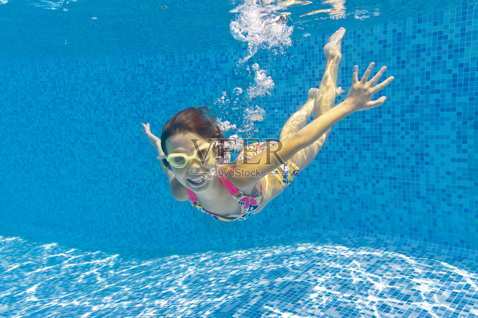 一个带着护目镜在游泳池里微笑着游泳的孩子照片摄影图片