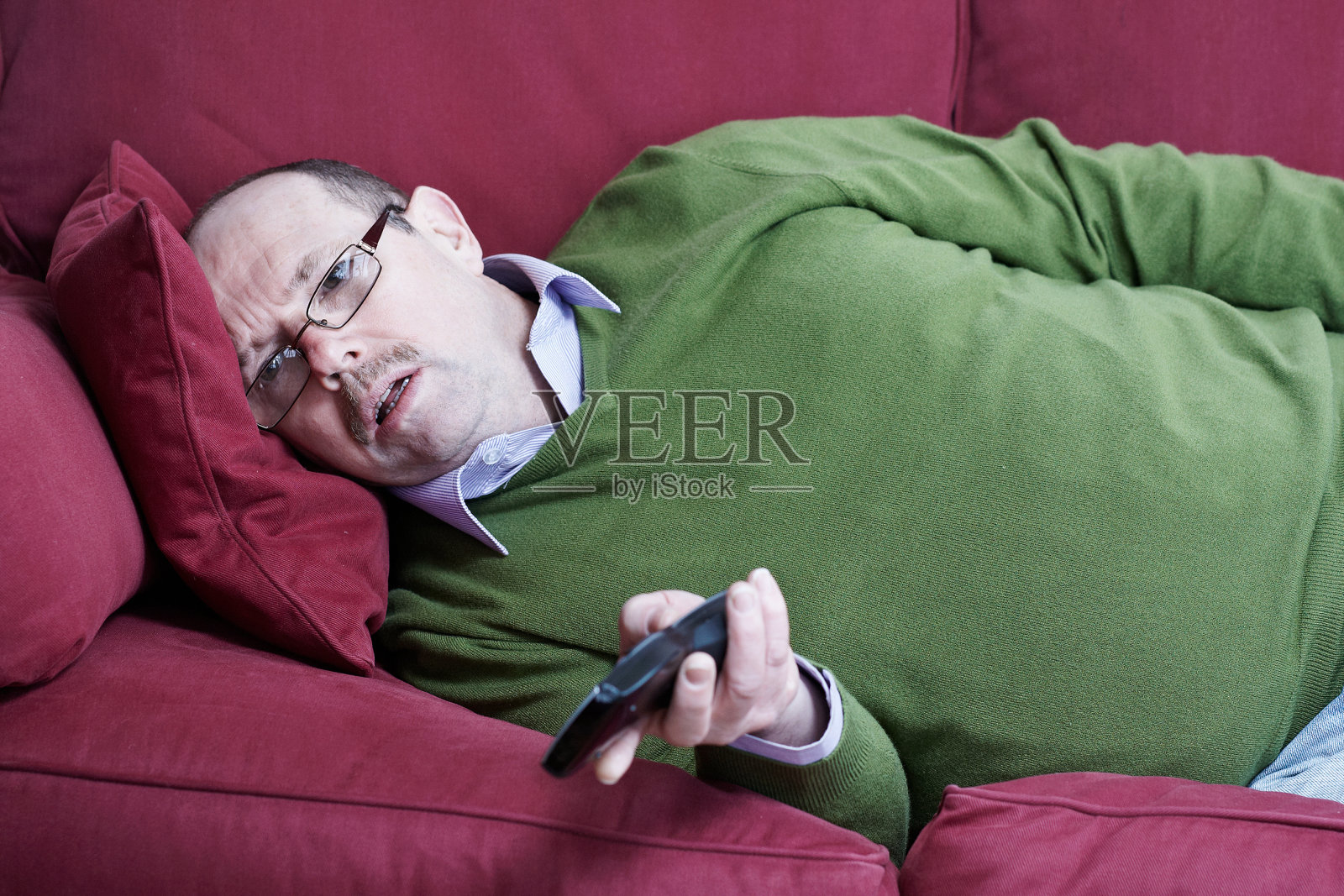 成熟男子肖像躺在沙发上与电视遥控器照片摄影图片