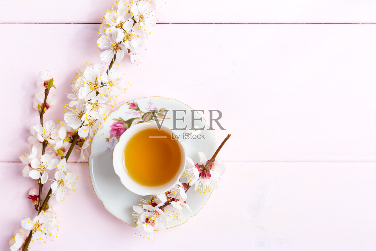 淡粉色的木桌上放着一杯茶和春花。照片摄影图片