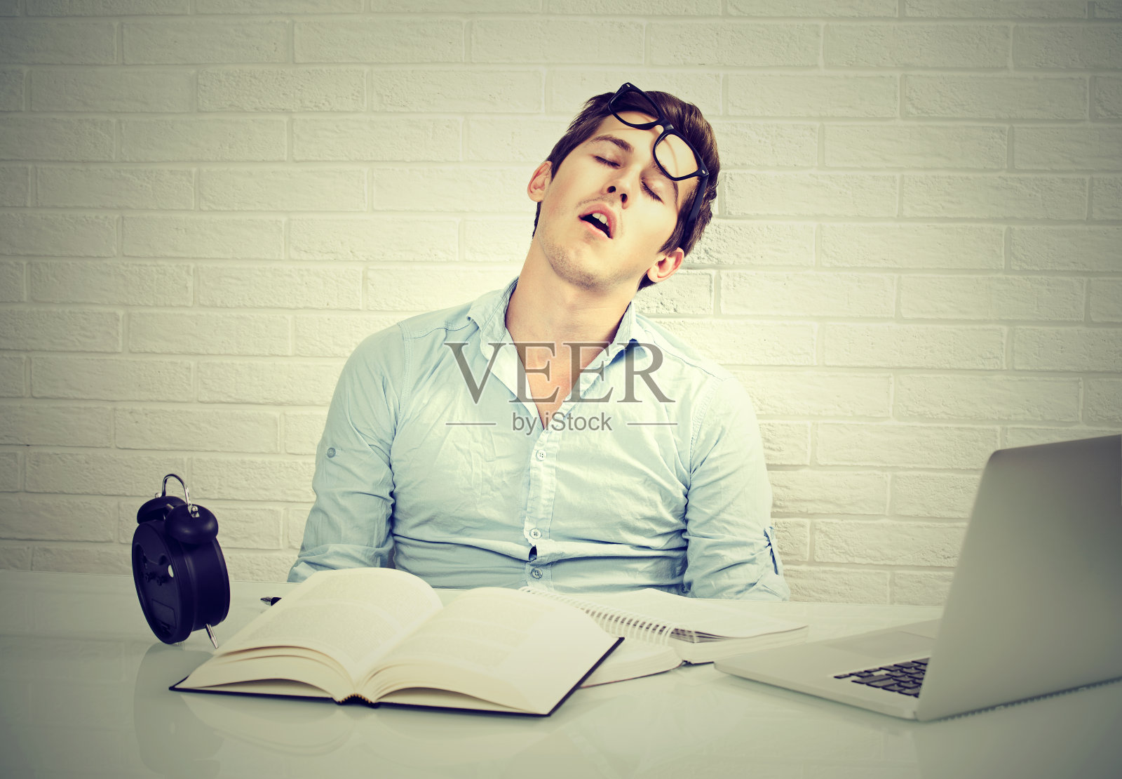 太多的工作使一个昏昏欲睡的年轻人坐在办公桌前照片摄影图片