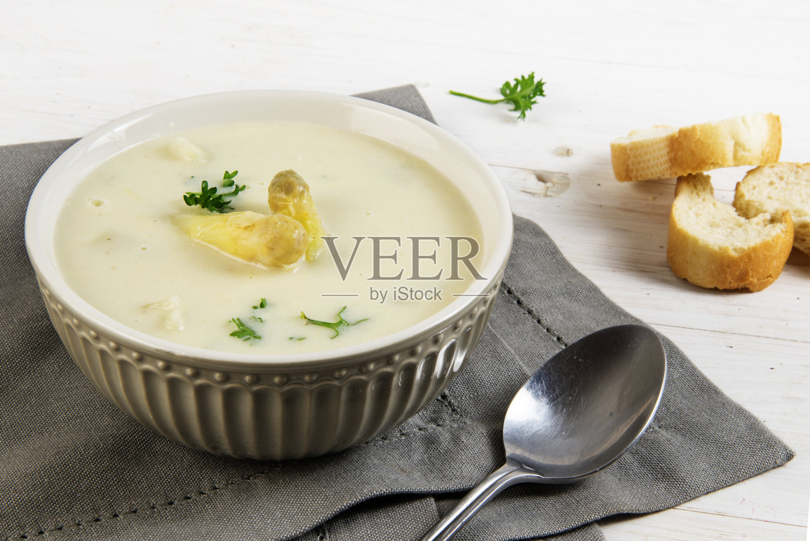 白芦笋奶油汤和欧芹装饰在碗和面包，灰色餐巾在白色的桌子上，复印空间照片摄影图片