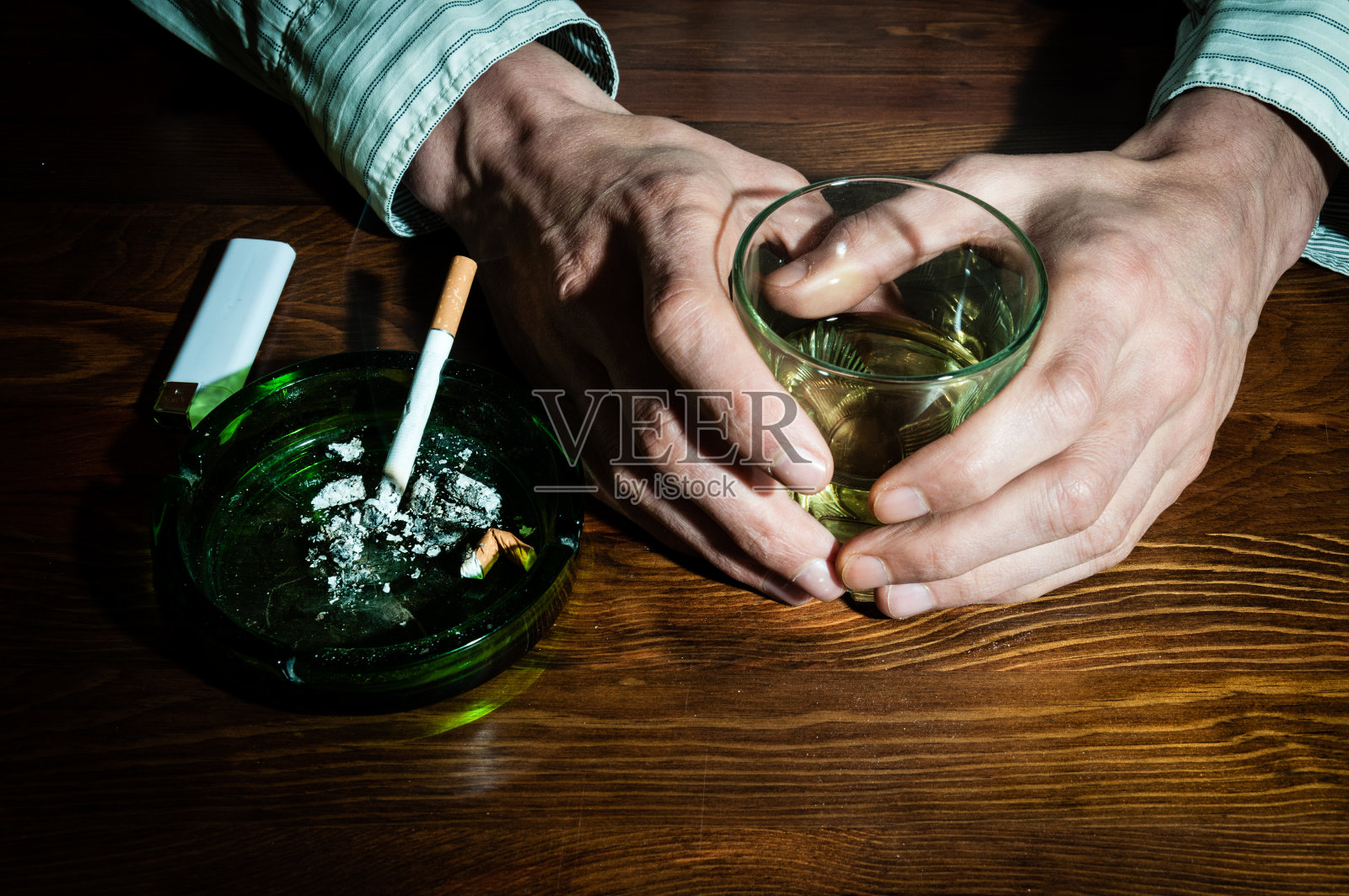 手握酒精饮料的男人与吸烟烟灰缸酒精饮料。照片摄影图片