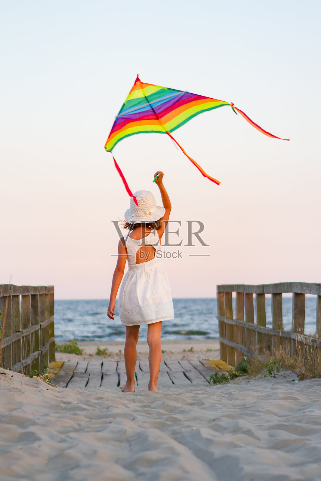 日落时分，女孩在海滩上玩彩虹彩色的风筝照片摄影图片