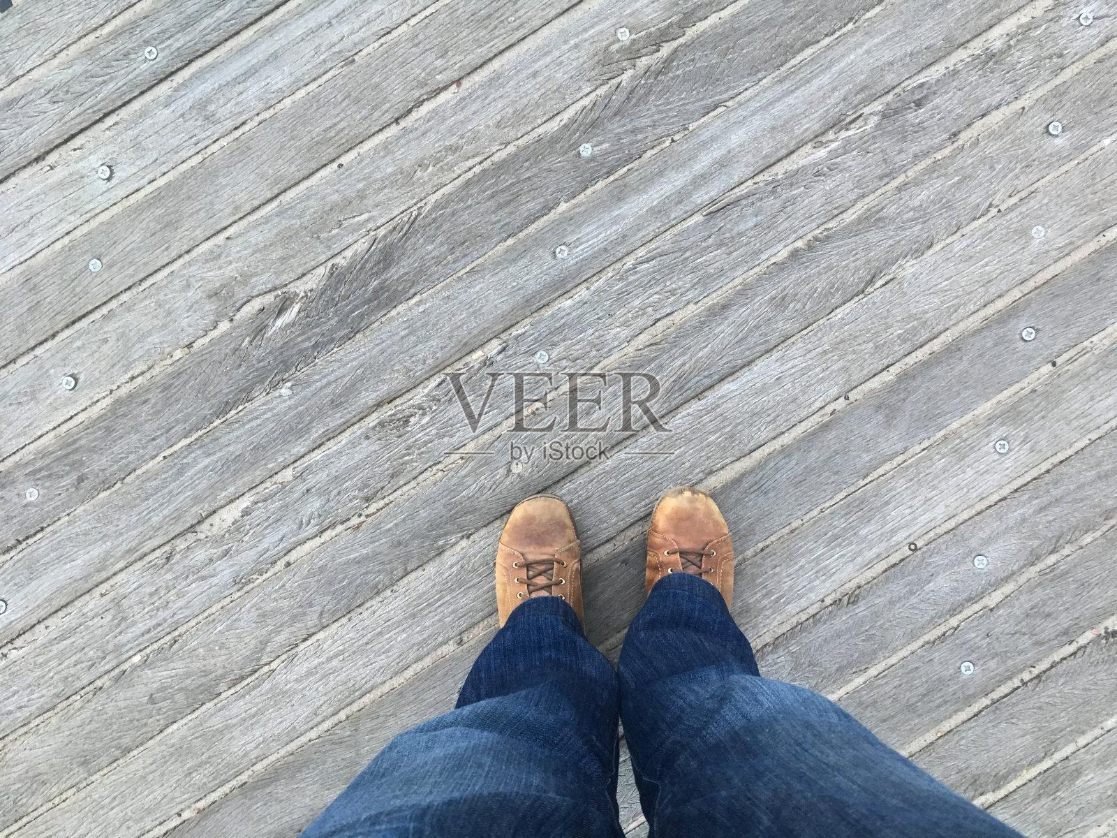站在纽约布鲁克林科尼岛的木板路上，从脚向下看。低头看着棕色的鞋子穿着粗布牛仔裤，站在外面的木码头上。照片摄影图片