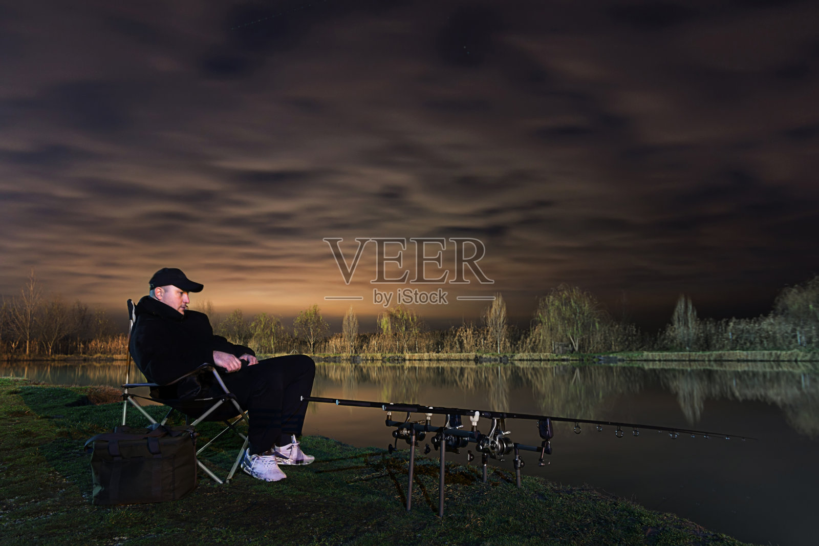 美丽夜晚的渔夫，坐在椅子上看钓竿照片摄影图片