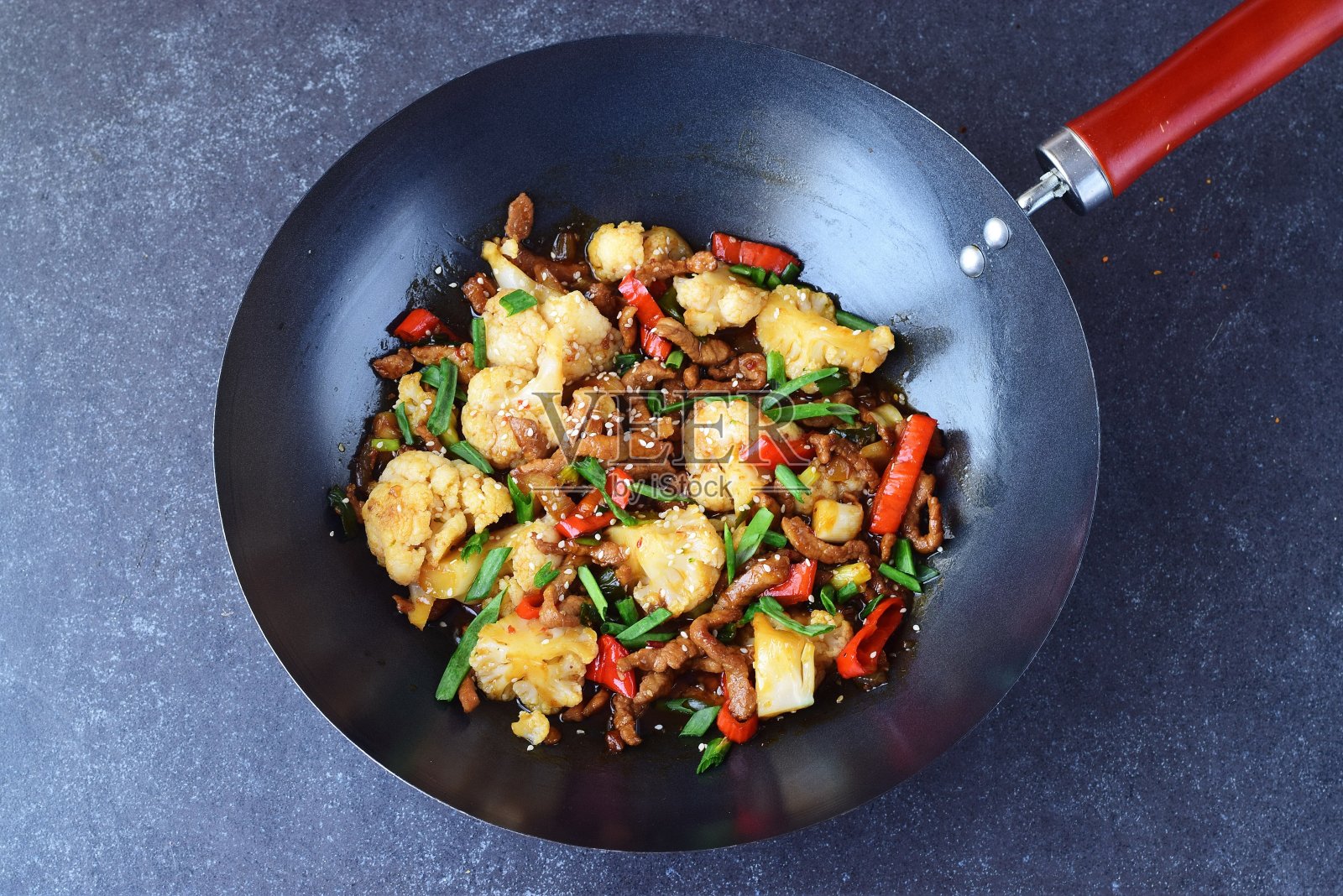 在灰色抽象的背景下，用花菜和蔬菜炒锅炒糖醋牛肉。东方菜肴。健康饮食的概念照片摄影图片