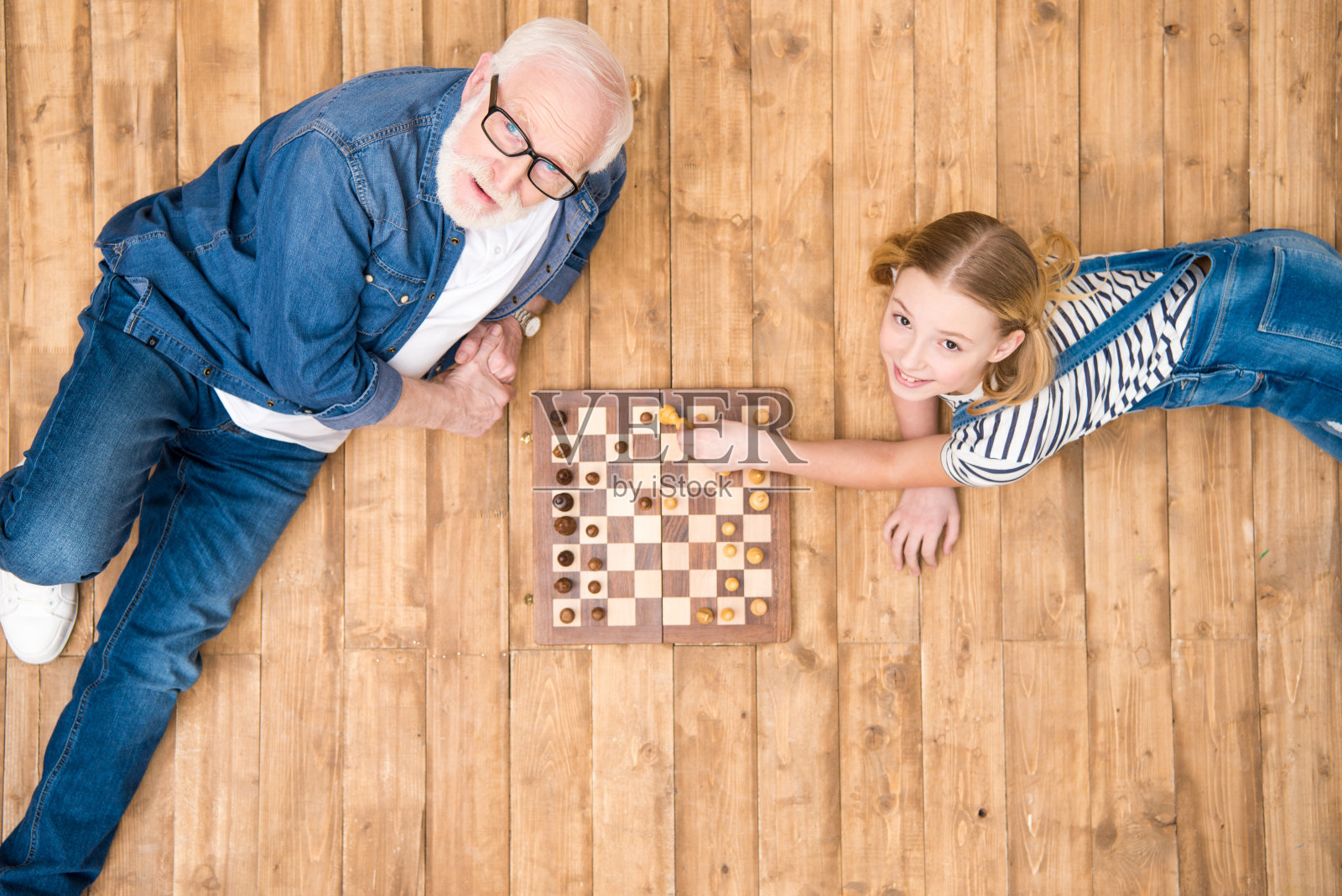 高角度的微笑女孩与高级男子下棋在木地板上照片摄影图片