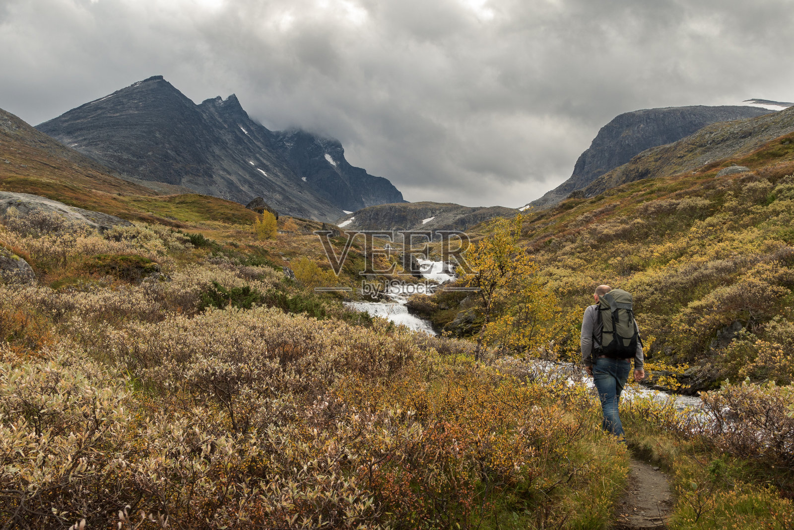 挪威约敦海门，一名男子独自沿着河流走向胡鲁甘山脉照片摄影图片
