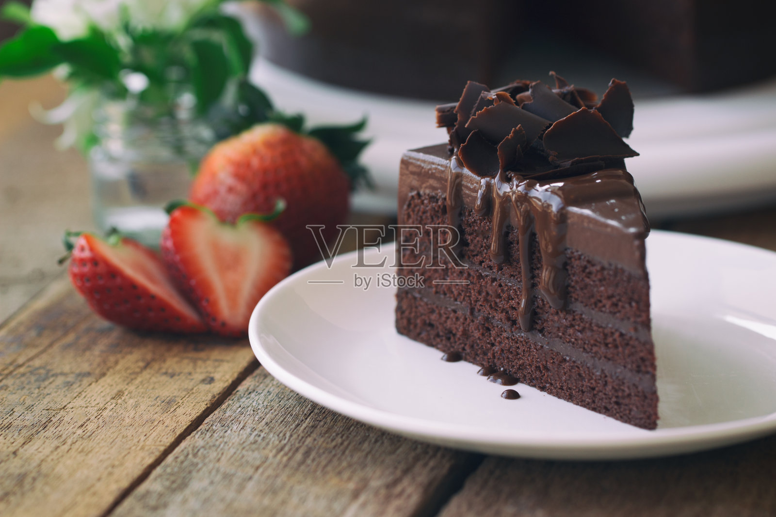 自制烘焙:用巧克力卷装饰的巧克力软糖蛋糕。咖啡、会议、茶点或茶点时间和生日聚会时，在质朴的木桌上放置三角形巧克力蛋糕。黑巧克力蛋糕背景和壁纸。照片摄影图片