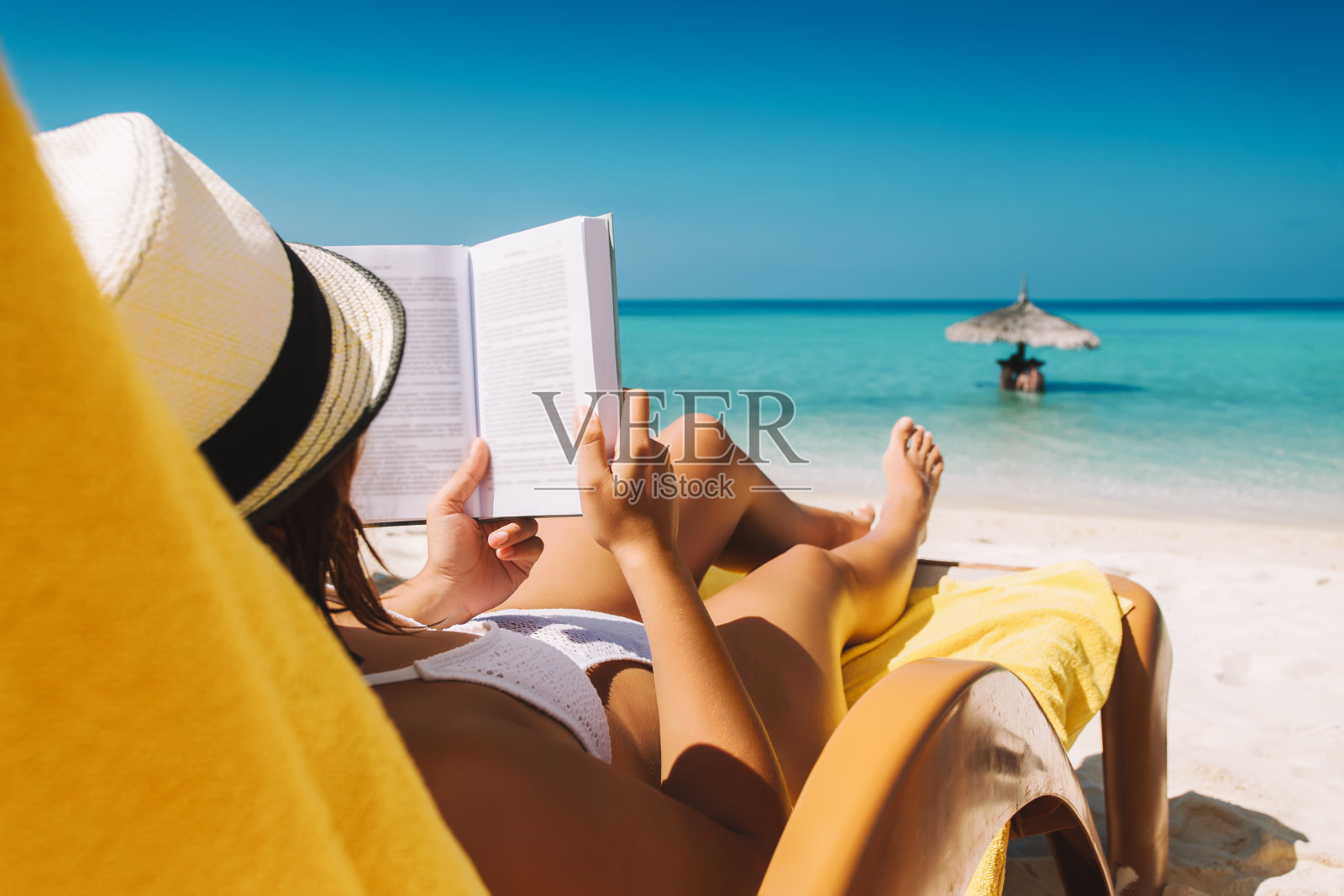 一名女子在热带岛屿的阳伞下躺在日光浴床上看书照片摄影图片