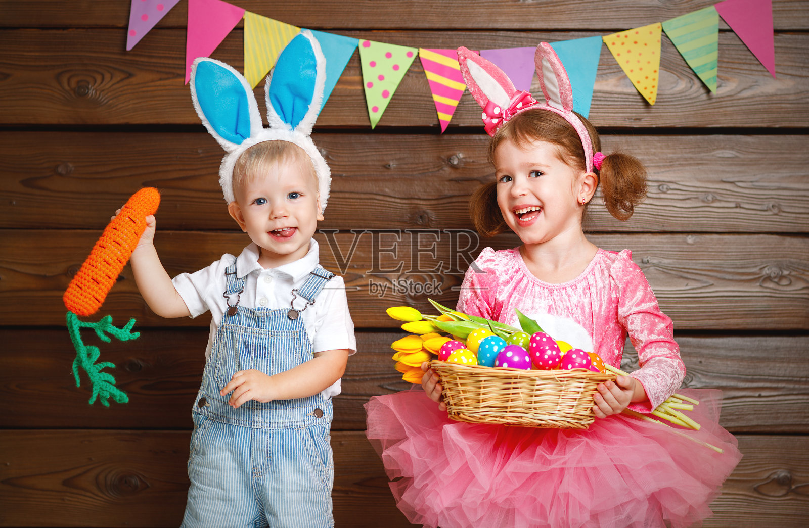 快乐的孩子们，男孩和女孩装扮成复活节兔子，用一篮子的鸡蛋放在木头上照片摄影图片