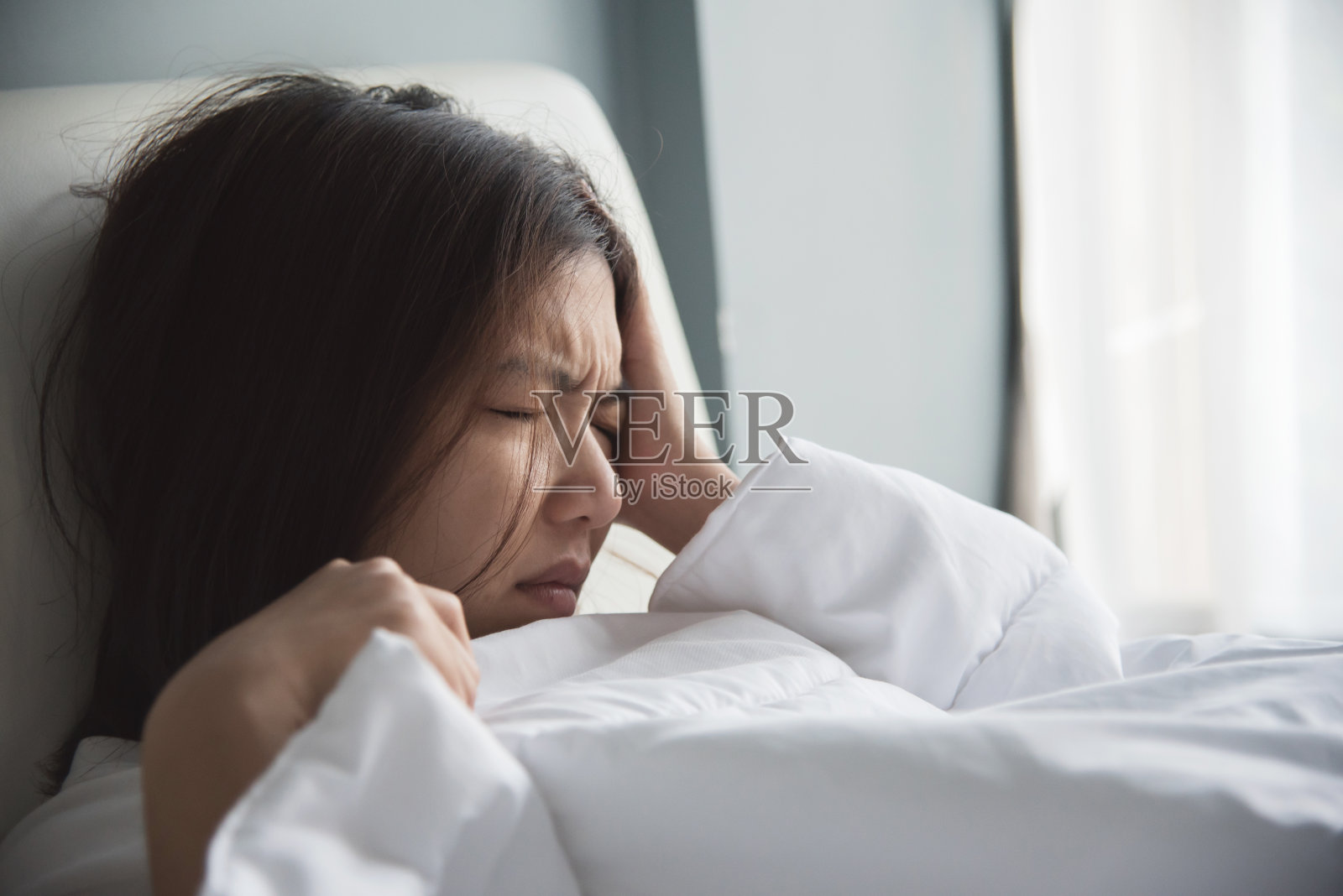 一位亚洲妇女在床上头痛。偏头痛。疾病,疾病的概念。照片摄影图片