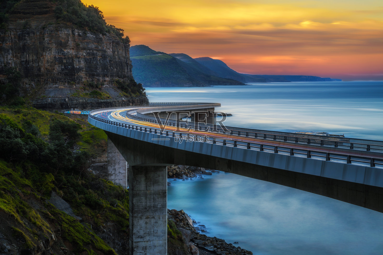 日落在海上悬崖桥沿澳大利亚太平洋海岸与过往的汽车灯光照片摄影图片