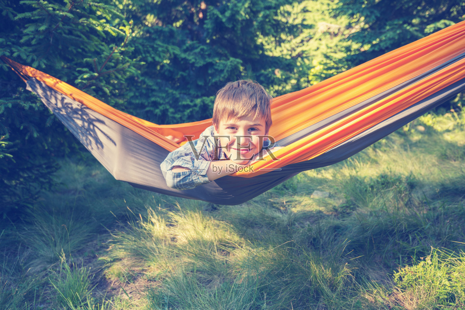 一个可爱的微笑男孩在林中空地的吊床上摇摆照片摄影图片