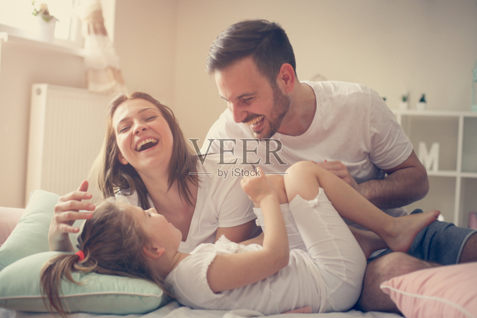 父母和他们的小女儿在床上玩得很开心。早上的家庭时光。照片摄影图片