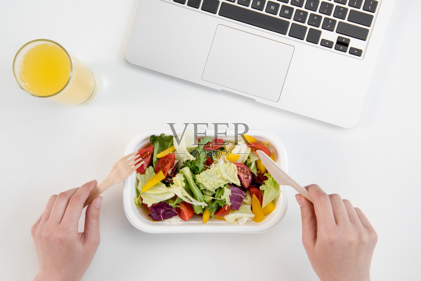 一个人在工作场所用笔记本电脑吃新鲜的沙拉和喝橙汁照片摄影图片