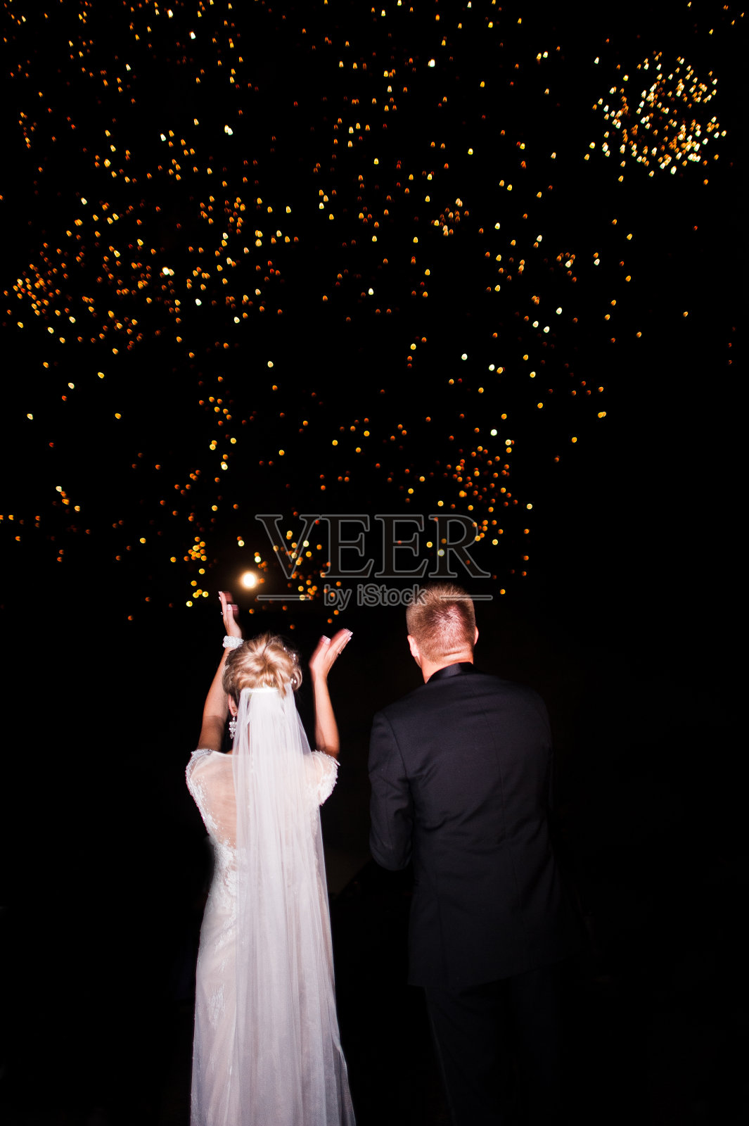 在新婚夫妇的背后，看着夜空和烟花。照片摄影图片